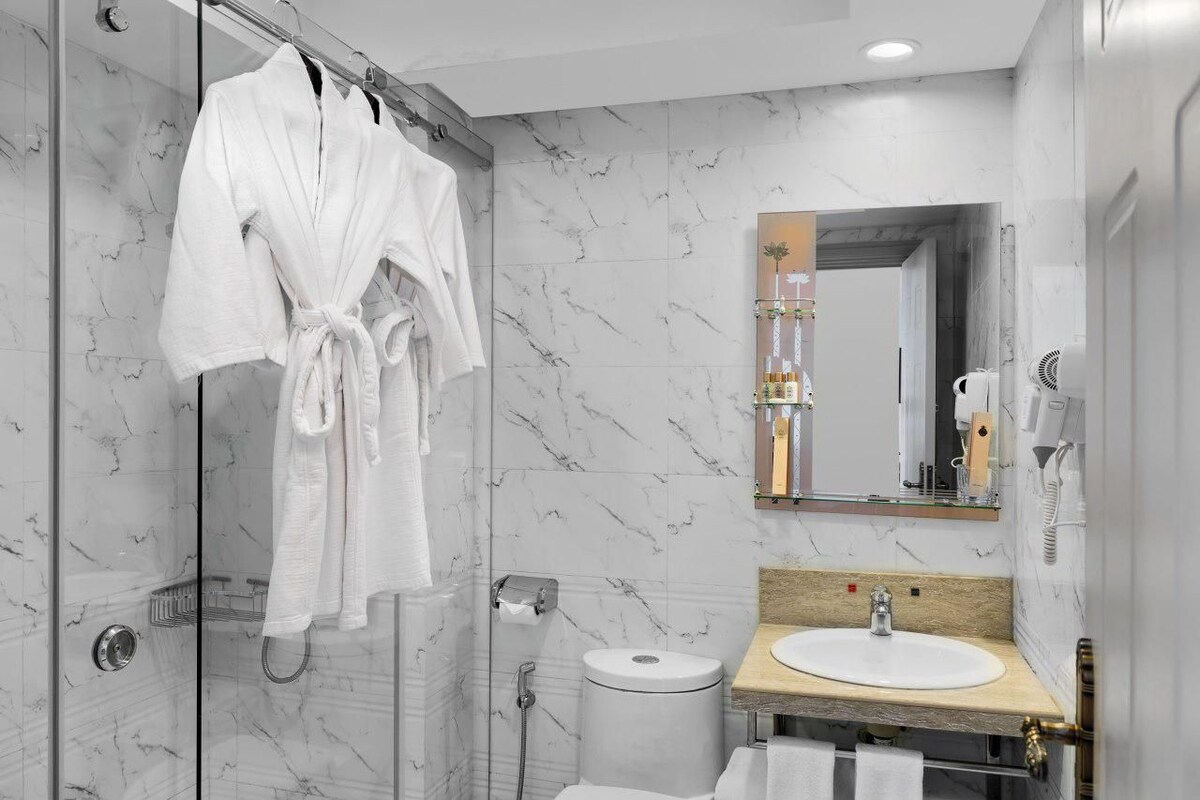 Un baño moderno con cabina de ducha de vidrio, pared con azulejos de mármol, tocador de madera con lavamanos y un espejo sobre el tocador.