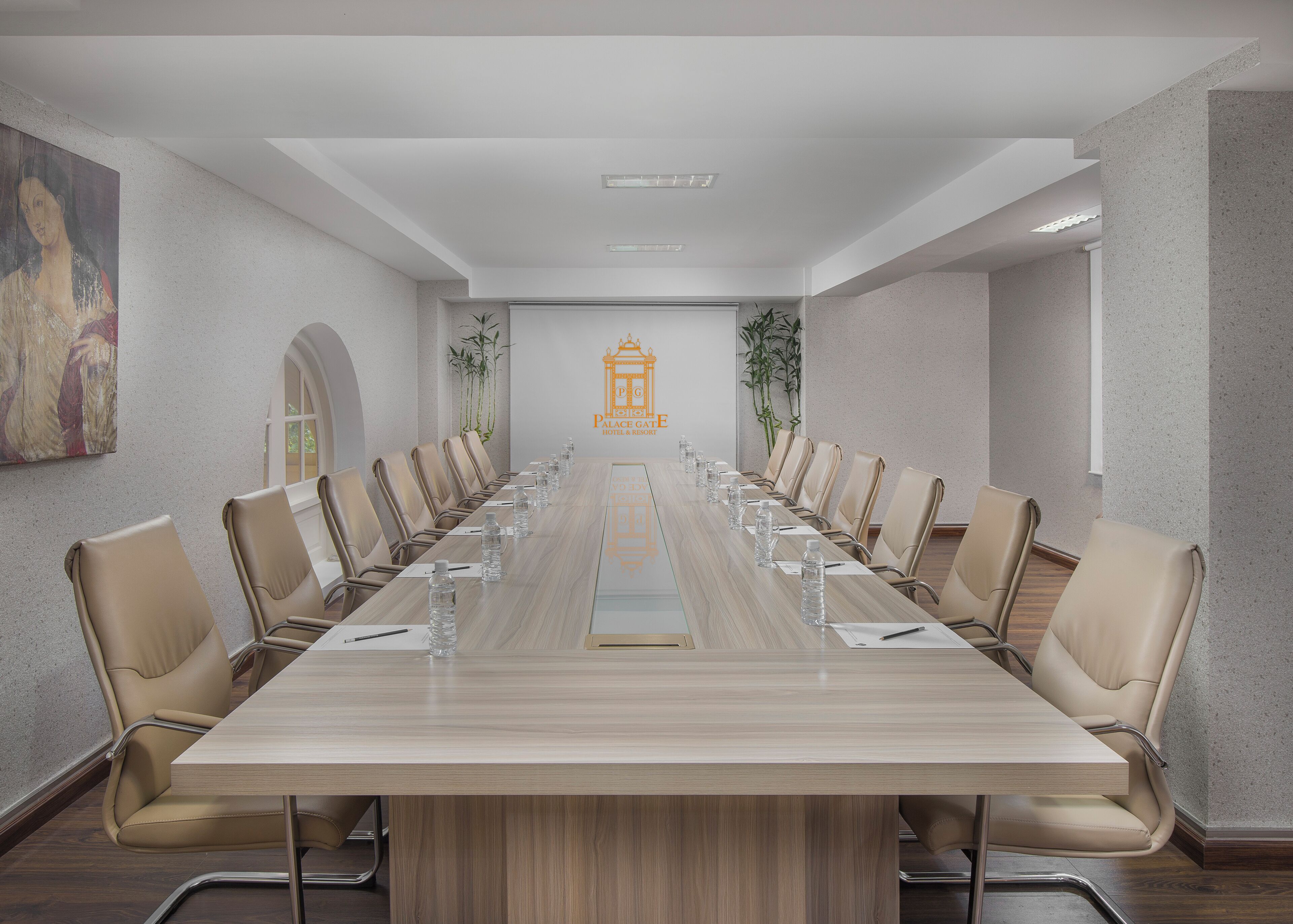 Ein Konferenzraum mit einem langen Tisch, beigen Stühlen, Wasserflaschen und einem Logo an der Wand.