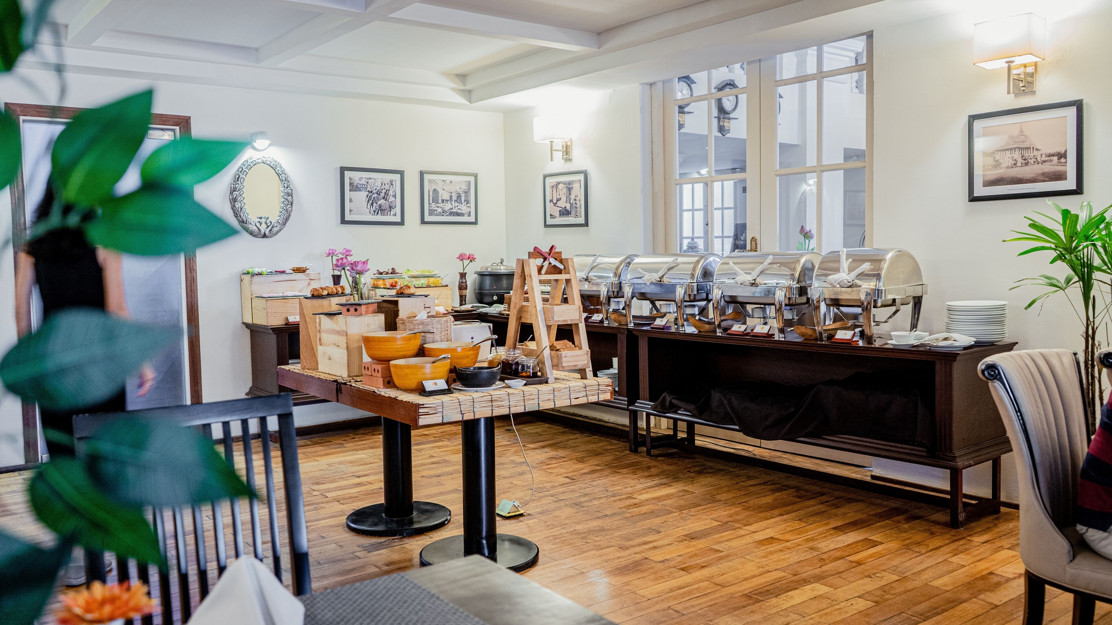 A buffet setup with various food stations, a wooden table with bowls and utensils, and a large window with a view of a building.