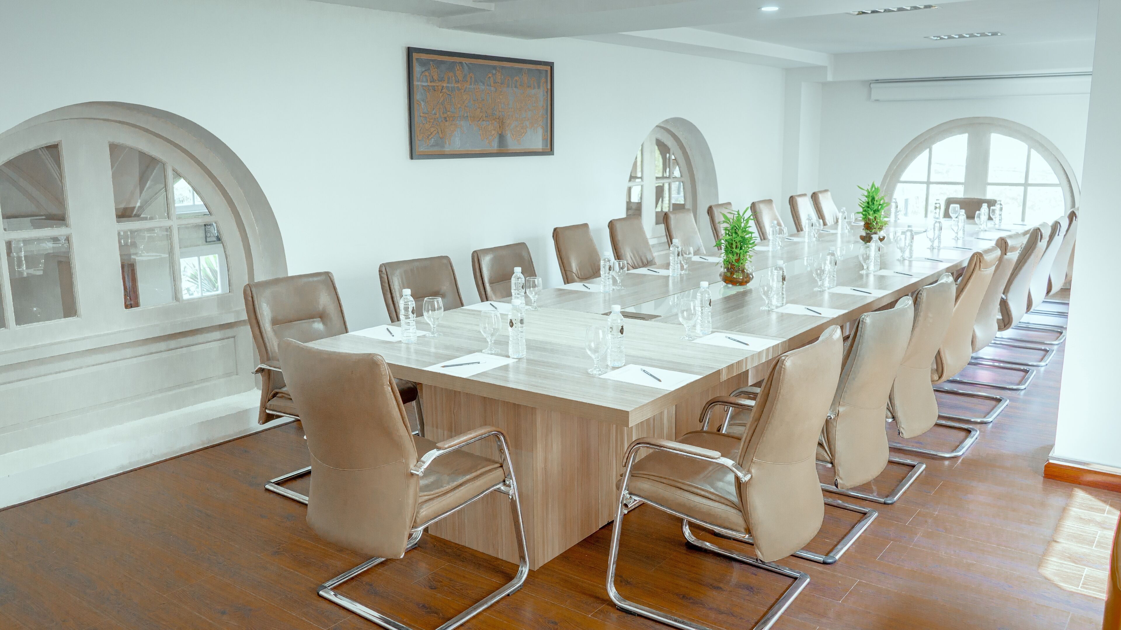 A conference room with a long table, beige chairs, and a potted plant.