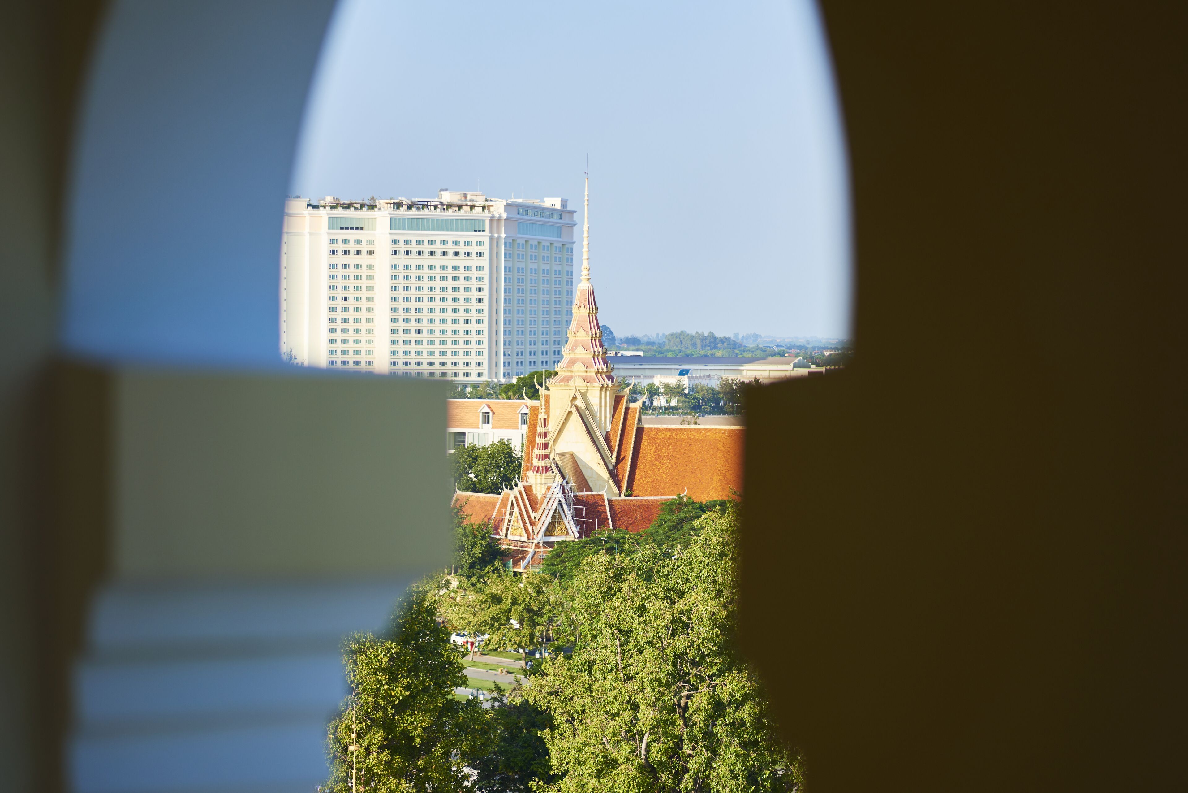 A view through a window of a building with a large white structure in the background and a traditional building with a pointed roof in the foreground.