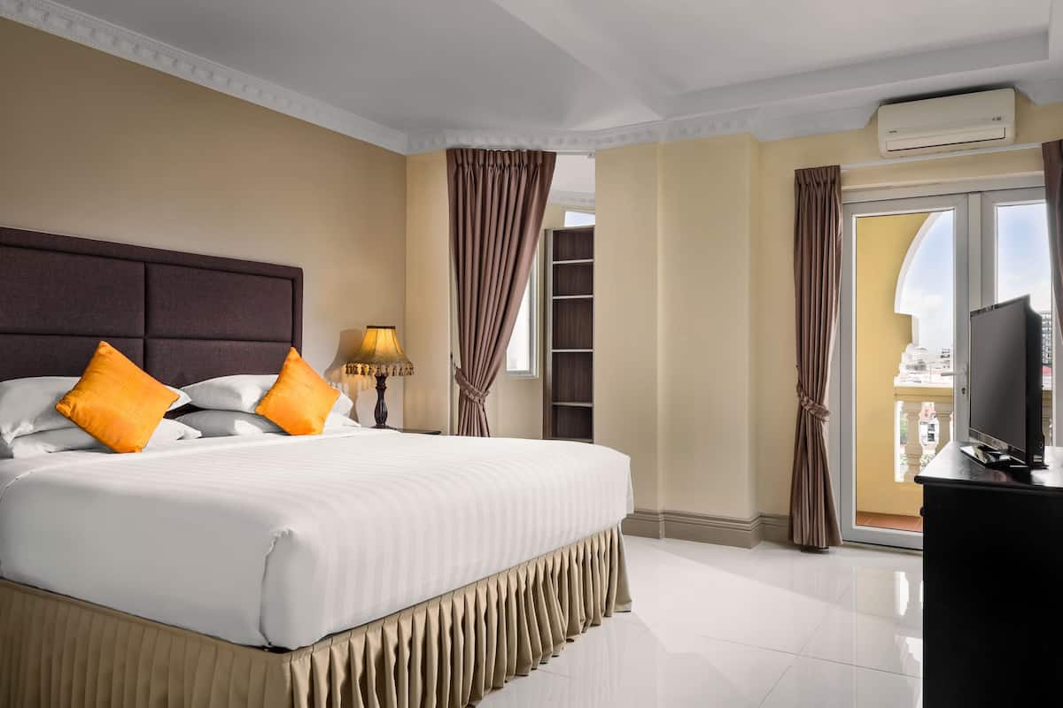 A hotel room with a large bed, a television, an air conditioning unit, and a balcony with curtains.