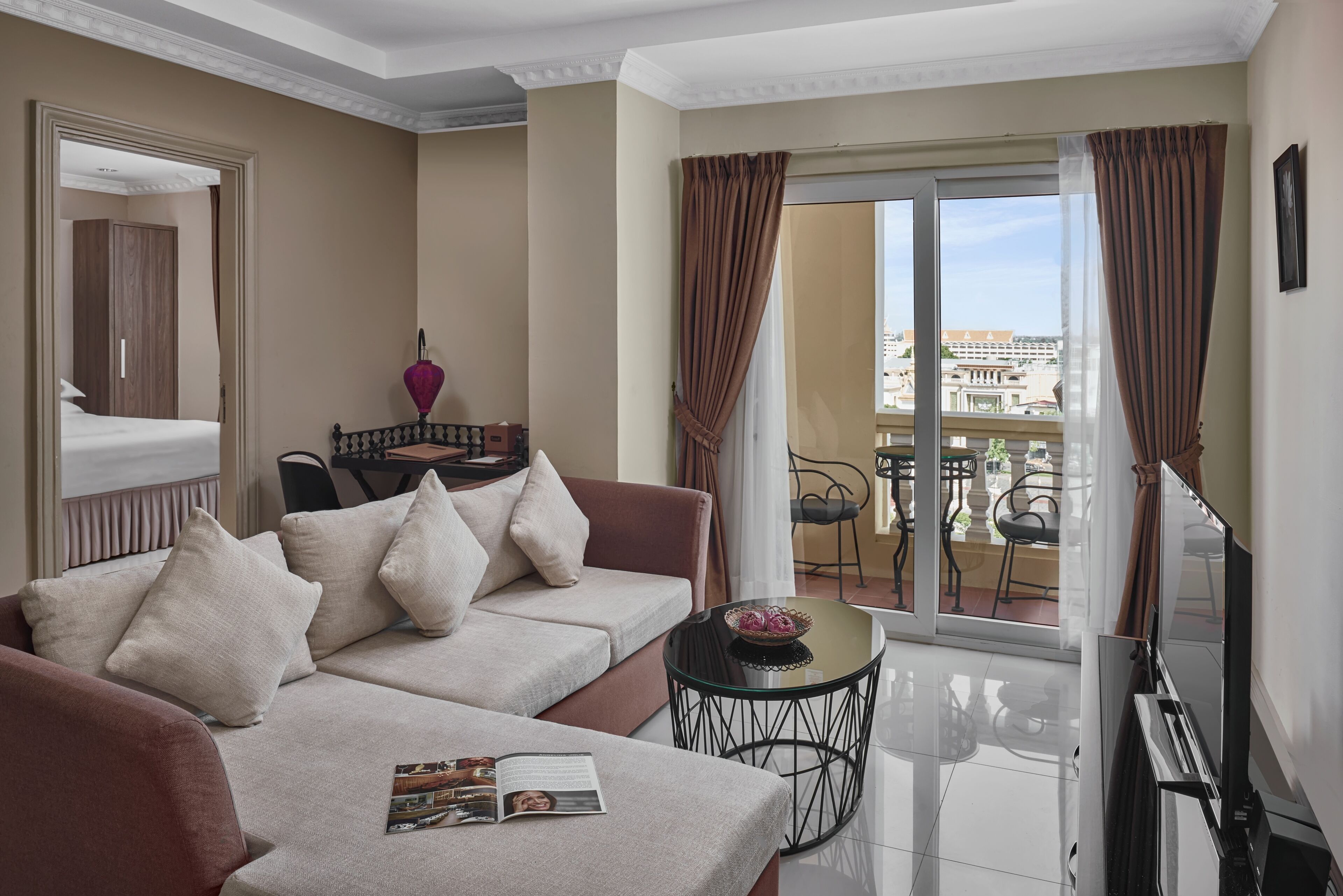 A modern living room with a sofa, a small table, and a balcony with a view of buildings.