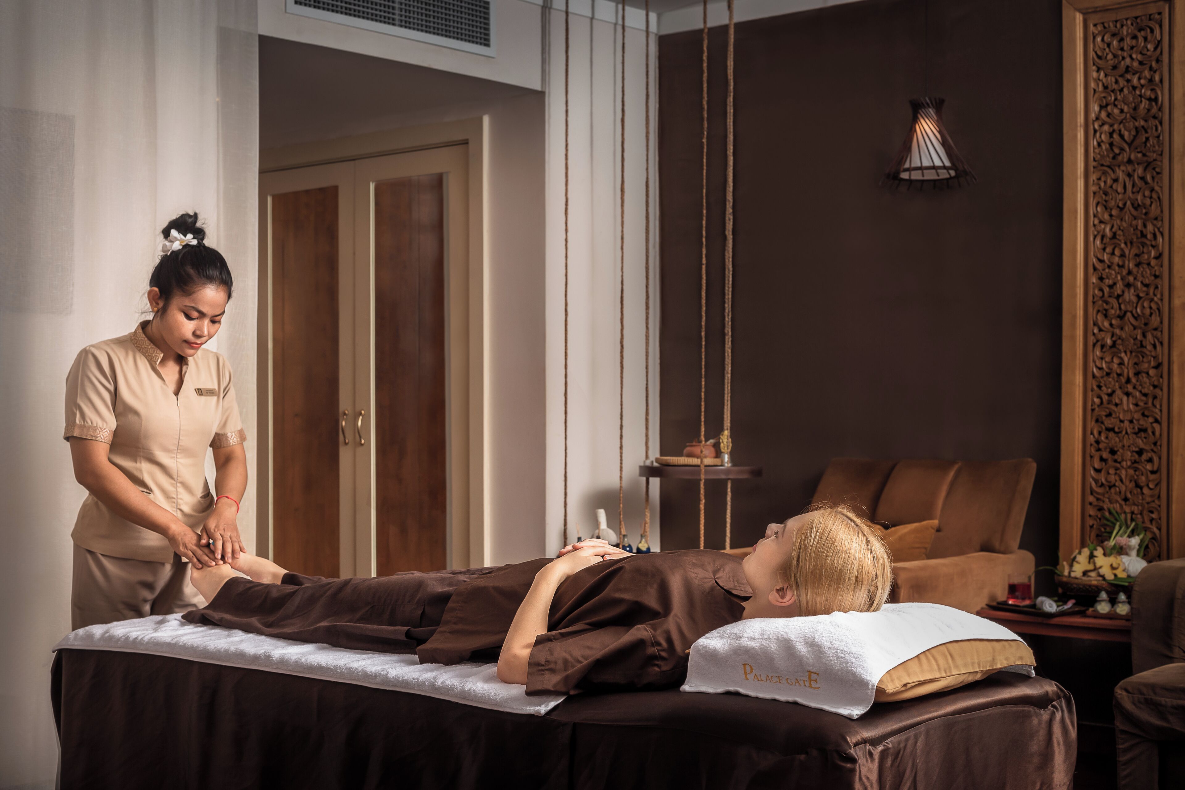 Een massageruimte met een massagetafel, een massagetherapeut en een ontspanningsruimte met een bank en decoratieve wandpanelen.