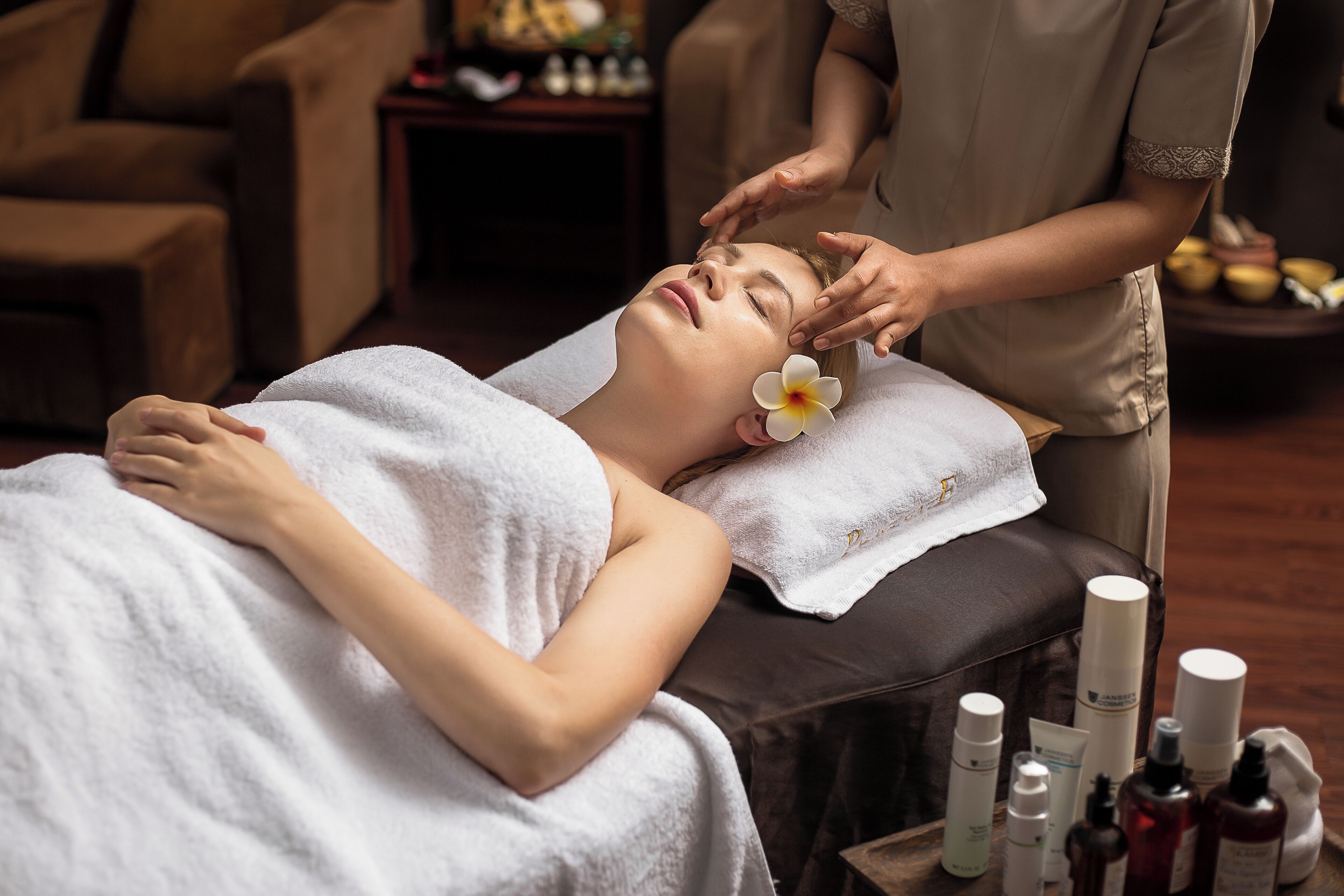 A person lying on a massage table with a towel, receiving a facial treatment.