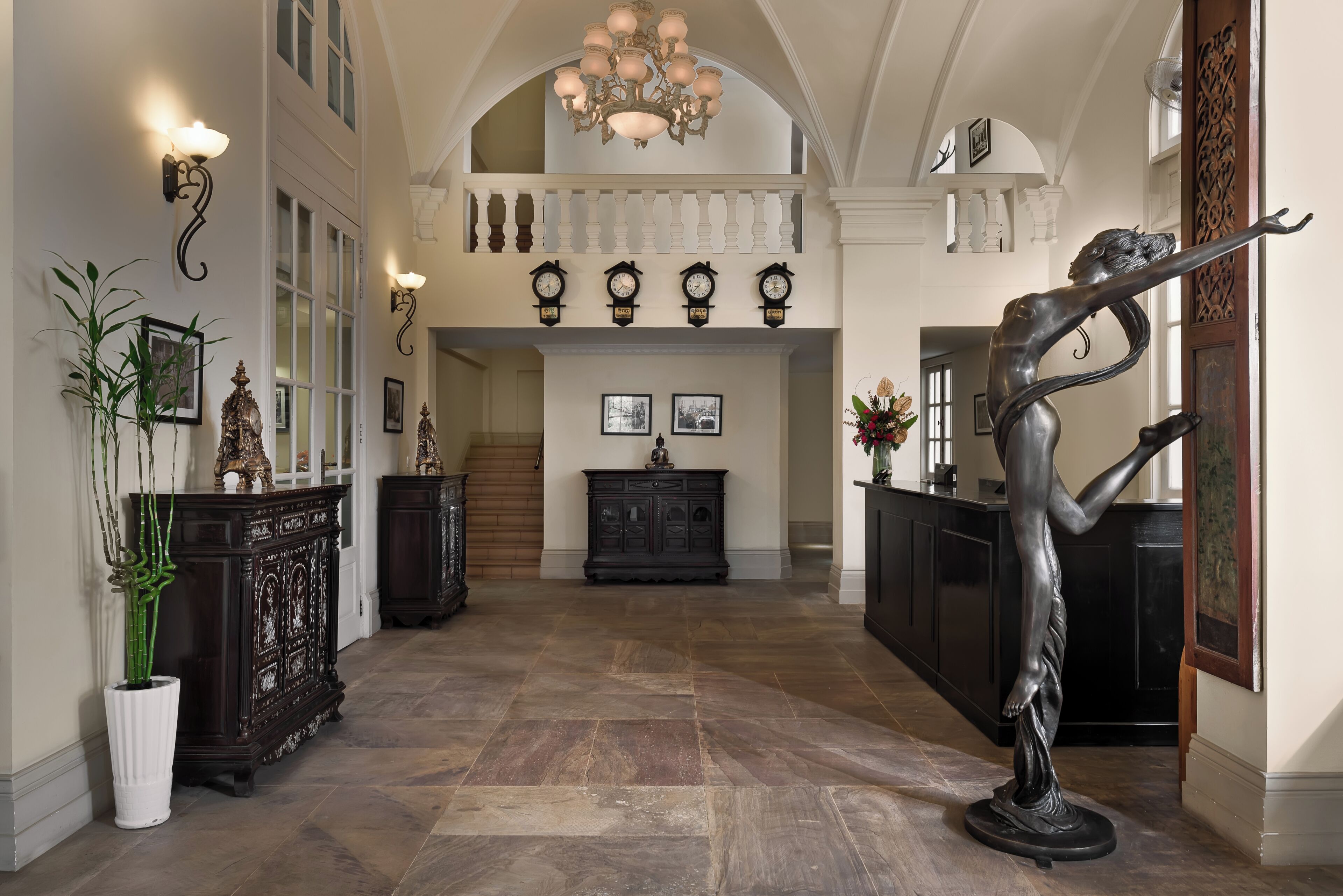 A grand hallway with a high ceiling, ornate wall sconces, and a large chandelier.