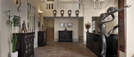 A grand hallway with a high ceiling, ornate wall sconces, and a large chandelier.