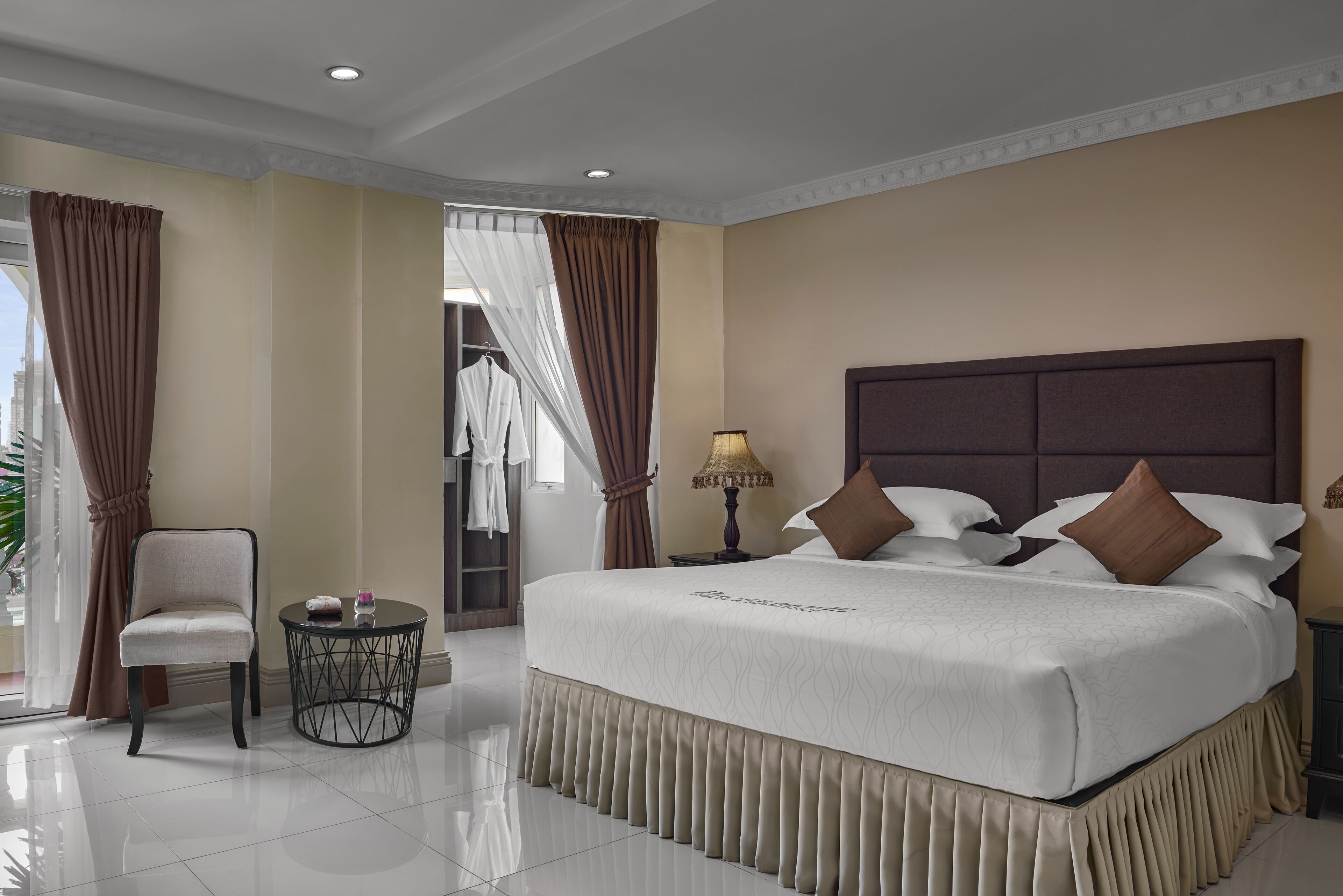 Habitación de hotel con una cama grande, una silla, una mesita y una lámpara.