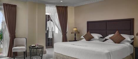 A hotel room with a large bed, a chair, a small table, and a lamp.