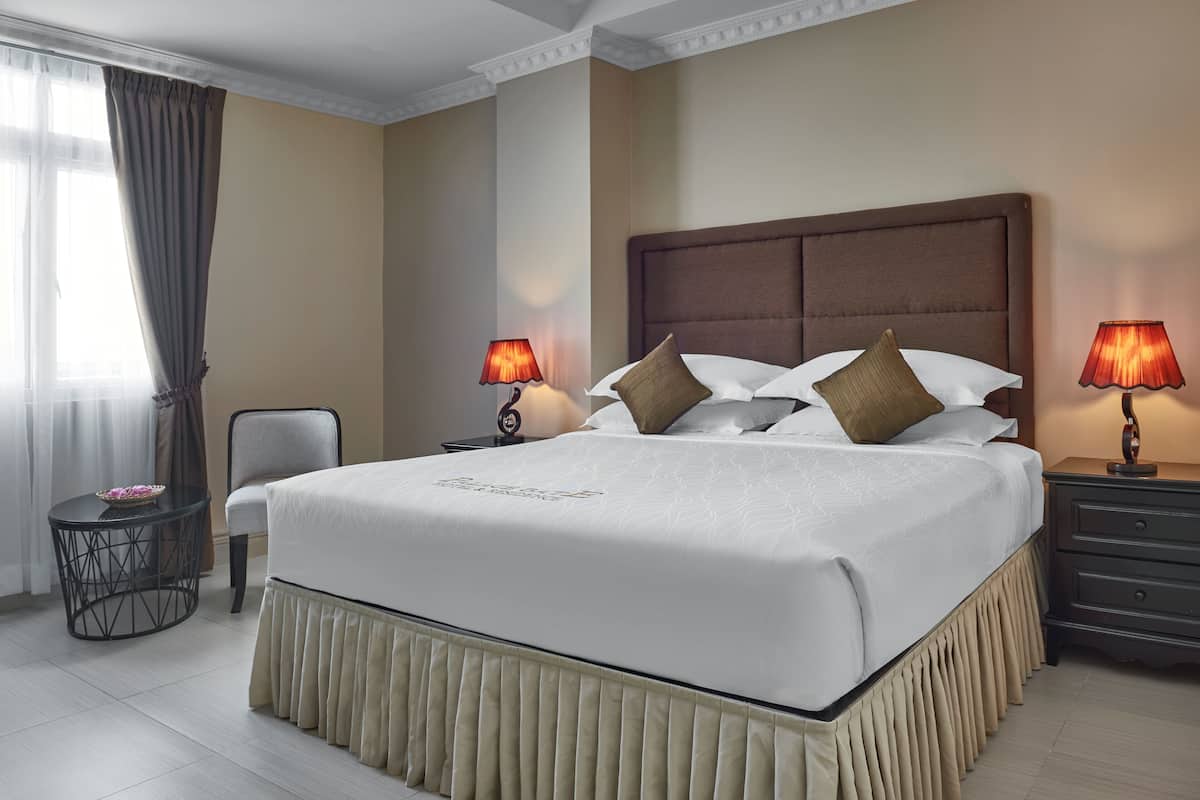 A hotel room with a large bed, two bedside tables with lamps, a chair, and a small table with a bowl of fruit.