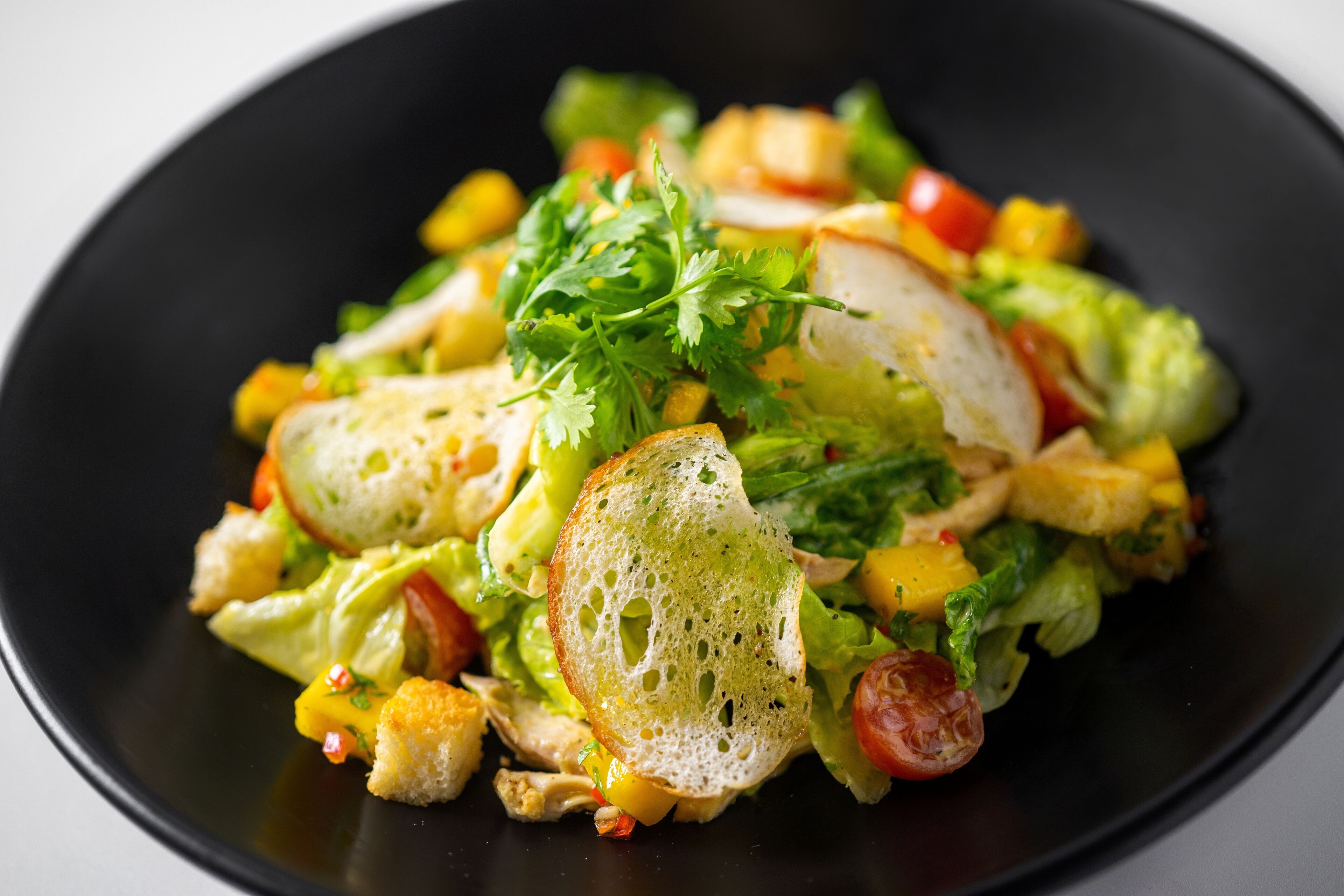 A salad with various vegetables and bread on a black plate.
