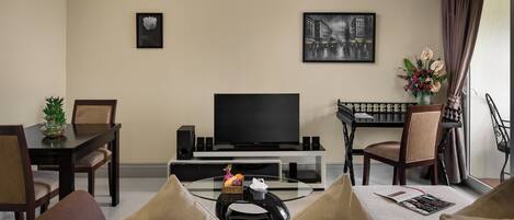 Una sala de estar con una televisión de pantalla plana, una mesa de comedor con sillas, un sofá y una mesa de centro con una revista.