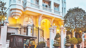 A yellow auto-rickshaw parked in front of a grand building with a balcony and large potted plants. - Palace Gate Hotel & Residence by EHM (Phnom Penh)