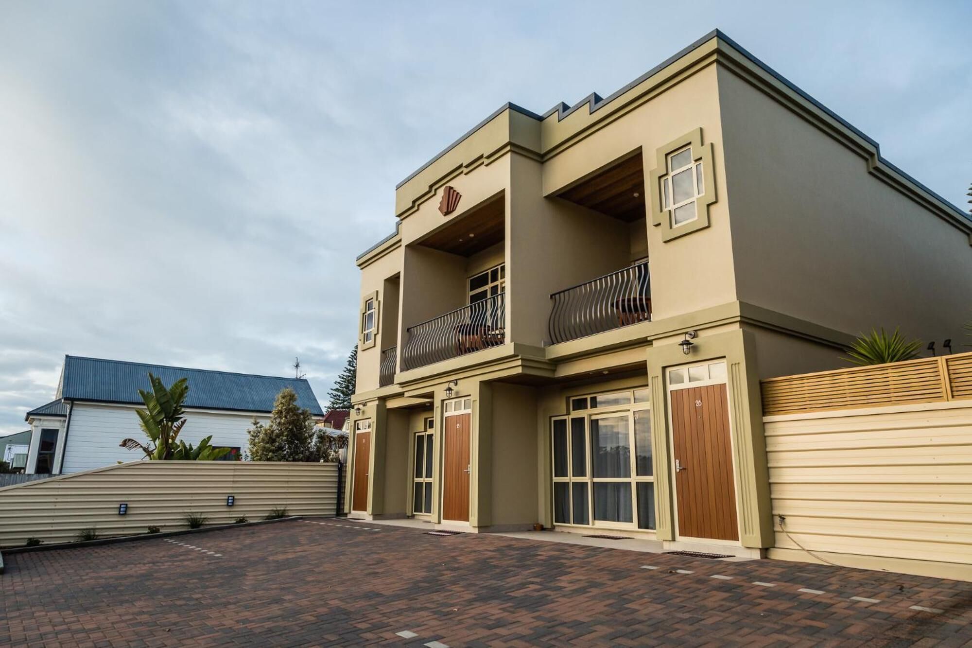A two-story building with a beige facade, large windows, and a balcony with a metal railing.