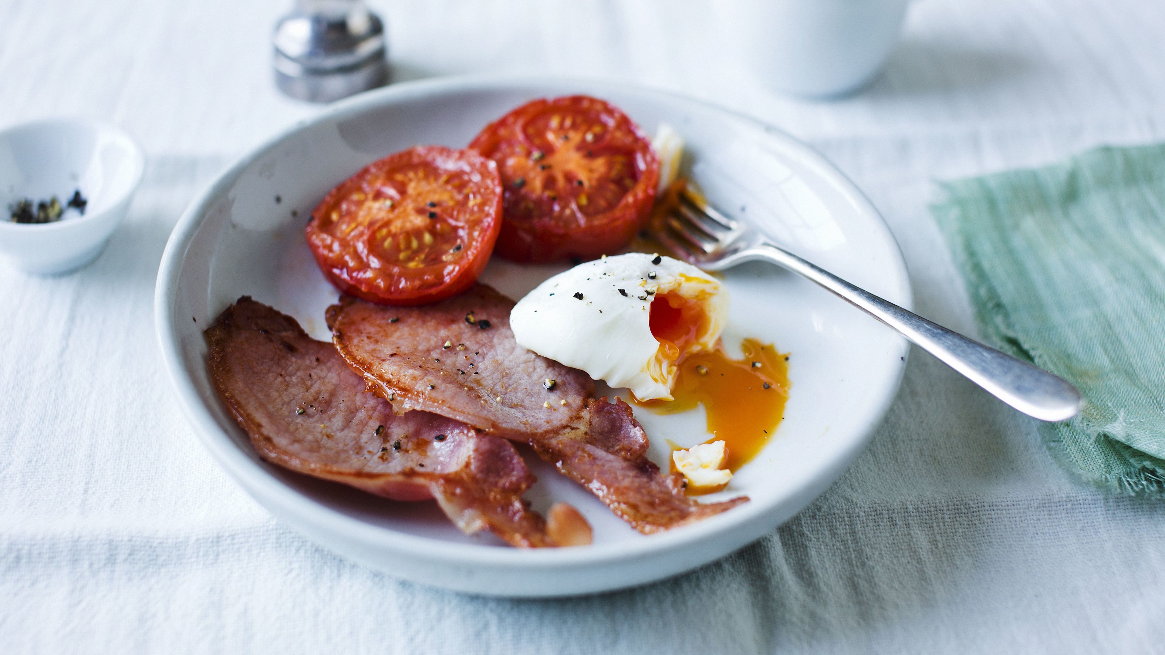 Un plato con tocino, un huevo pochado y rodajas de tomate.