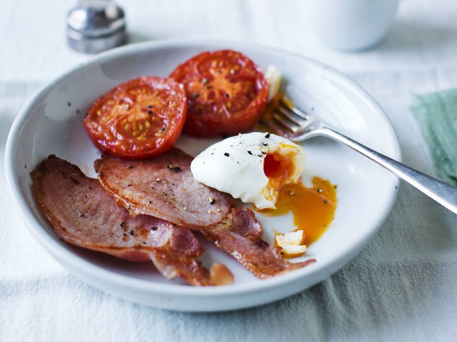 Um prato com bacon, ovo pochê e tomates fatiados.