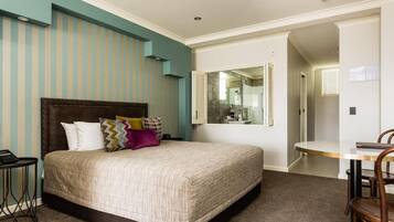 A bedroom with a large bed, a bedside table, a chair, a desk, and a bathroom visible through an open door.