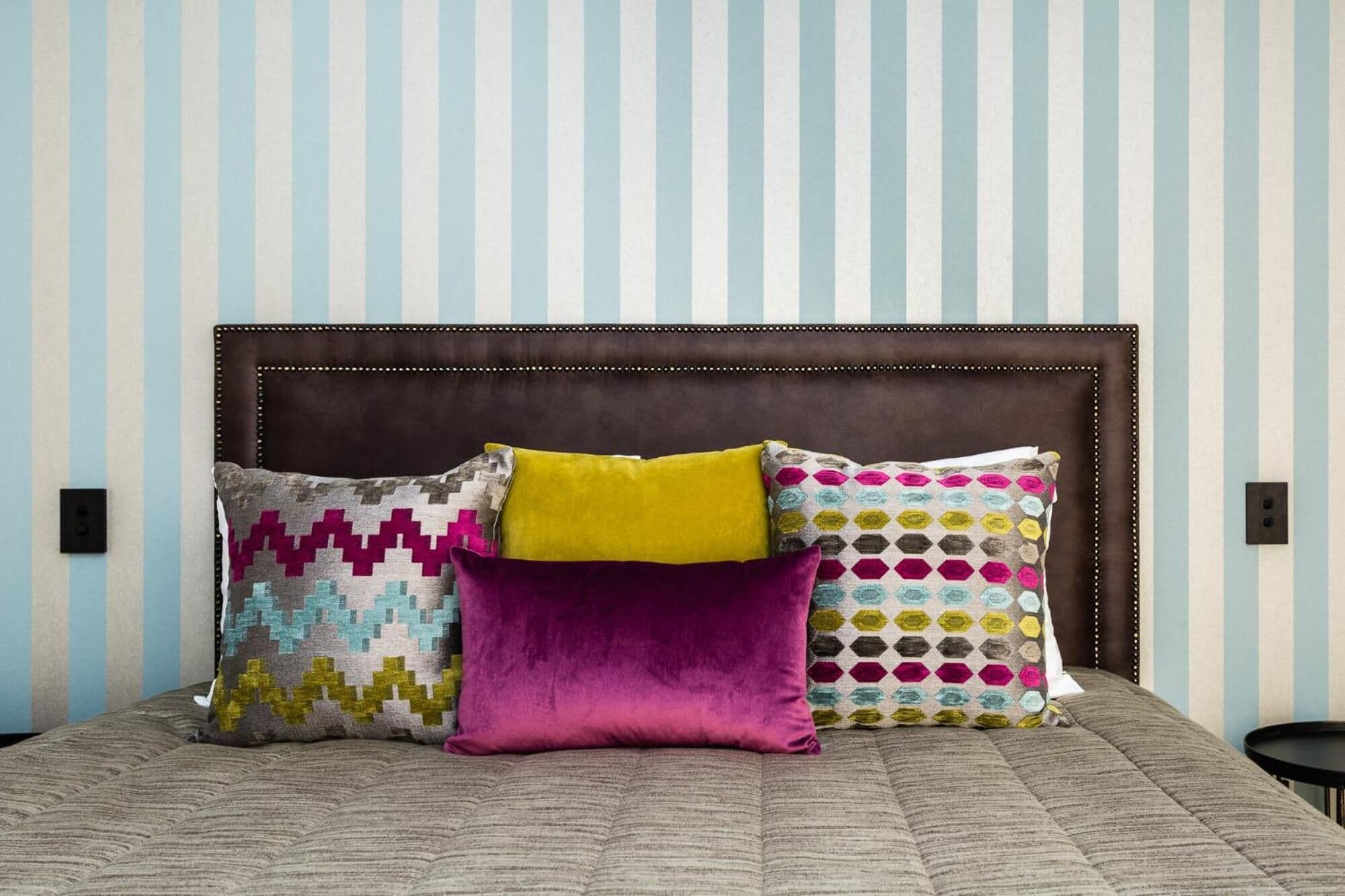 Un lit avec une tête de lit marron et quatre oreillers aux motifs et couleurs variés.