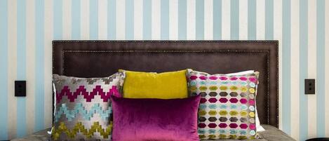 Un lit avec une tête de lit marron et quatre oreillers aux motifs et couleurs variés.