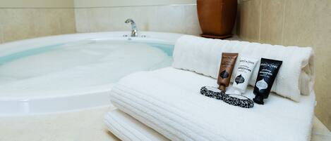 A bathroom with a bathtub, a potted plant, and toiletries on a towel.