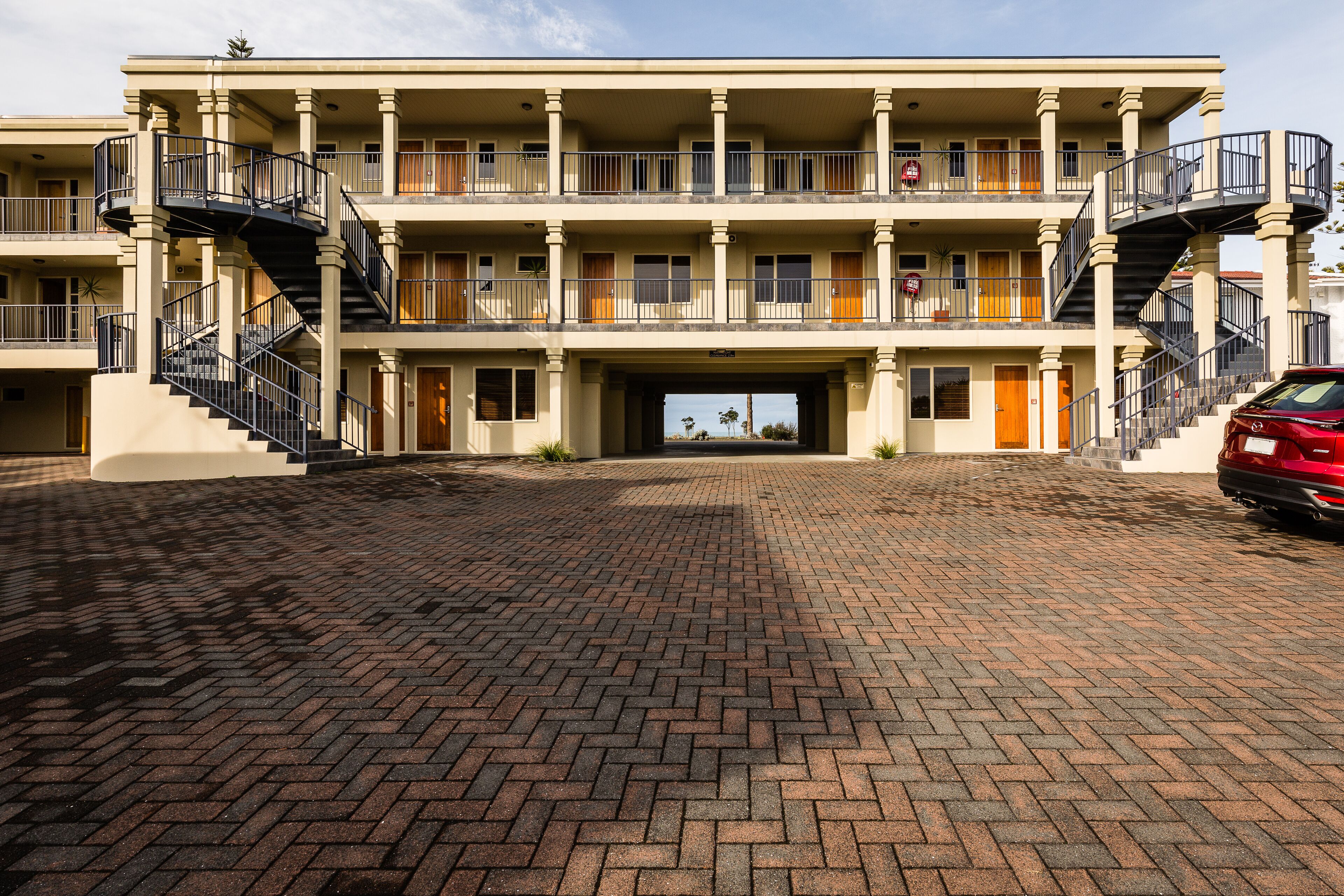 A multi-story hotel with a brick-paved entrance, balconies, and a red car parked outside.