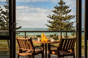 A wooden table with two chairs and a breakfast setup on a balcony overlooking a scenic view of the ocean and trees.