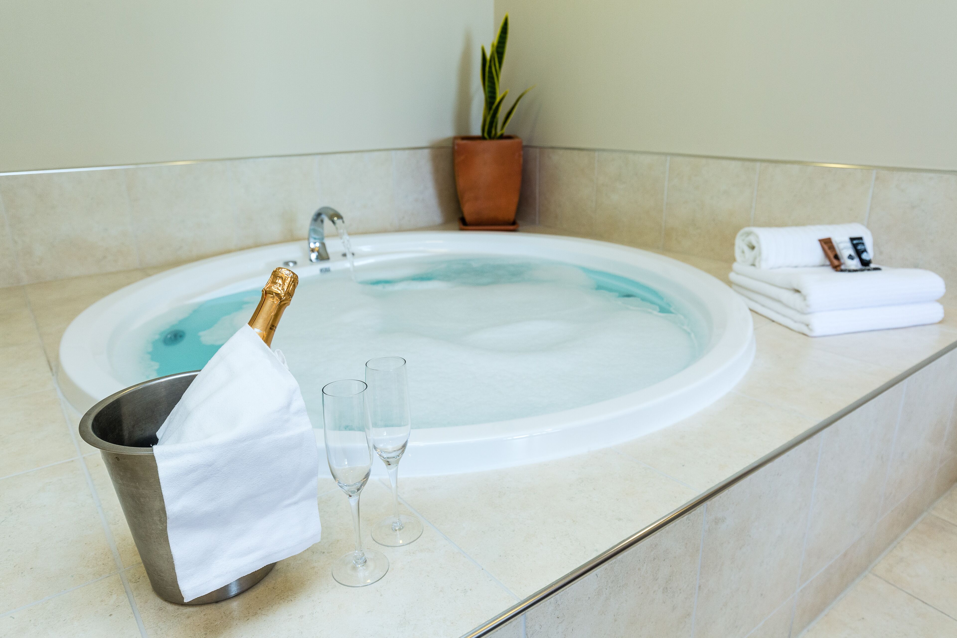 Una vasca da bagno con una bottiglia di champagne, due bicchieri e un asciugamano su un ripiano piastrellato.