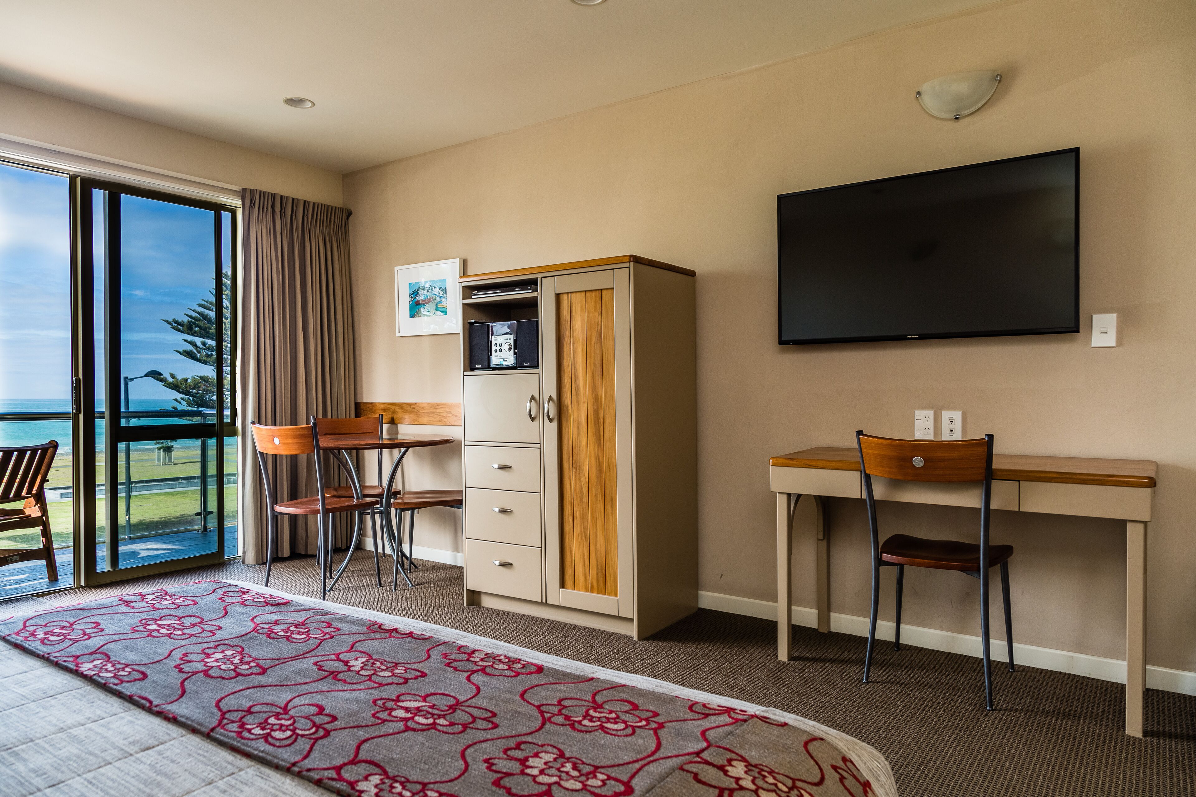 A hotel room with a bed, a desk, a chair, a wardrobe, a television, and a view of the outdoors.