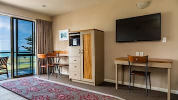 A hotel room with a bed, a desk, a chair, a wardrobe, a television, and a view of the outdoors.