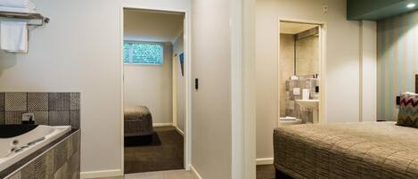 A hotel room with a bed, a small seating area, a bathroom with a sink and toilet, and a window with blinds.