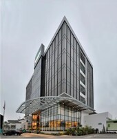 A modern hotel with a glass facade, a prominent entrance canopy, and a flagpole in the foreground.