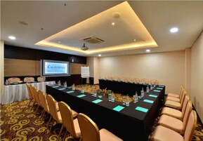 A conference room with a long table, chairs, a projector screen, and a carpeted floor.