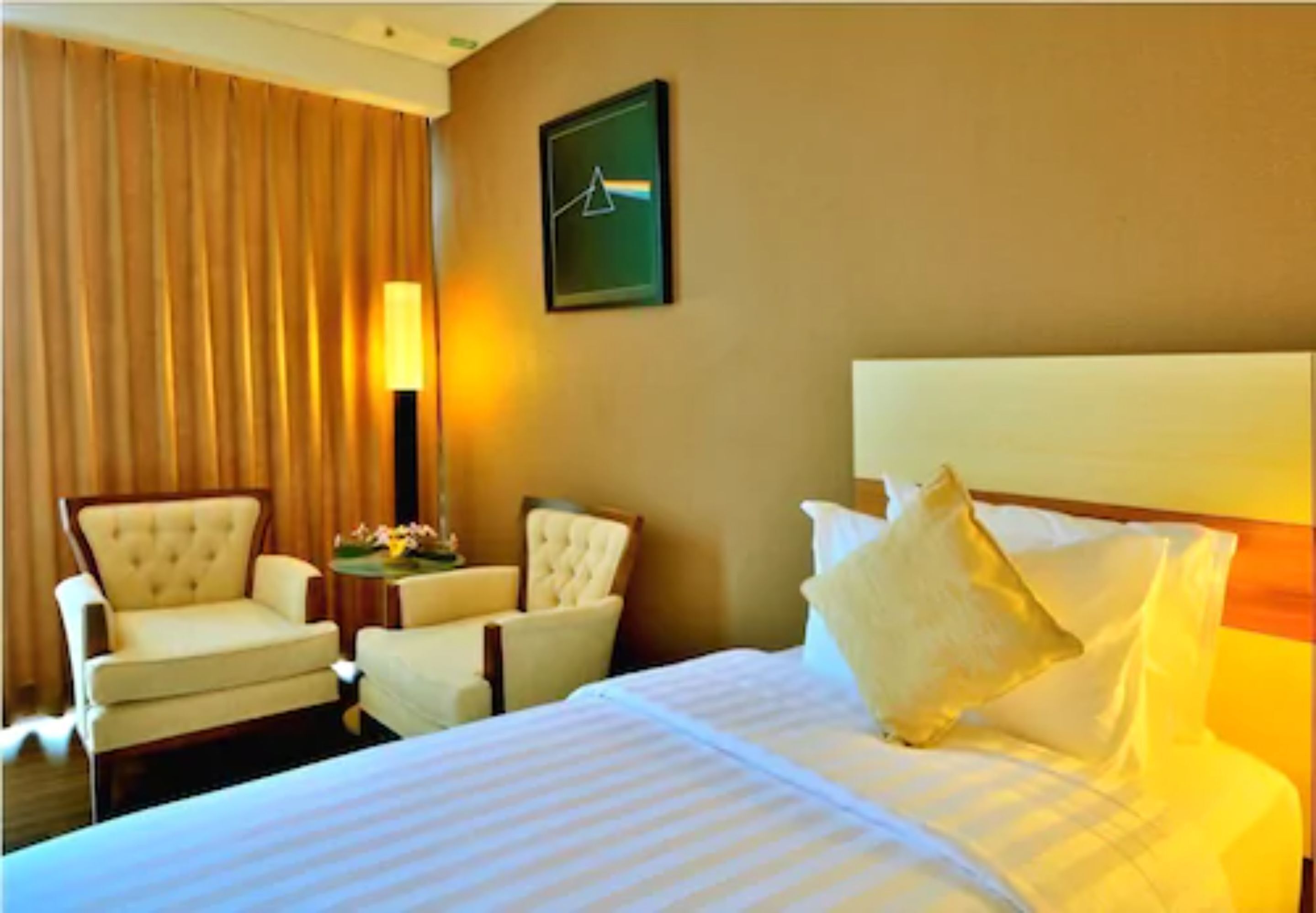 A hotel room with a large bed, two armchairs, a side table, and a lamp.