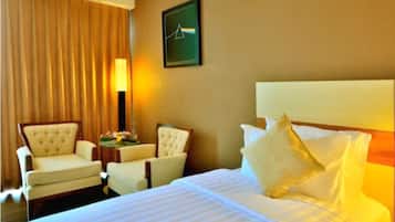 A hotel room with a large bed, two armchairs, a side table, and a lamp.