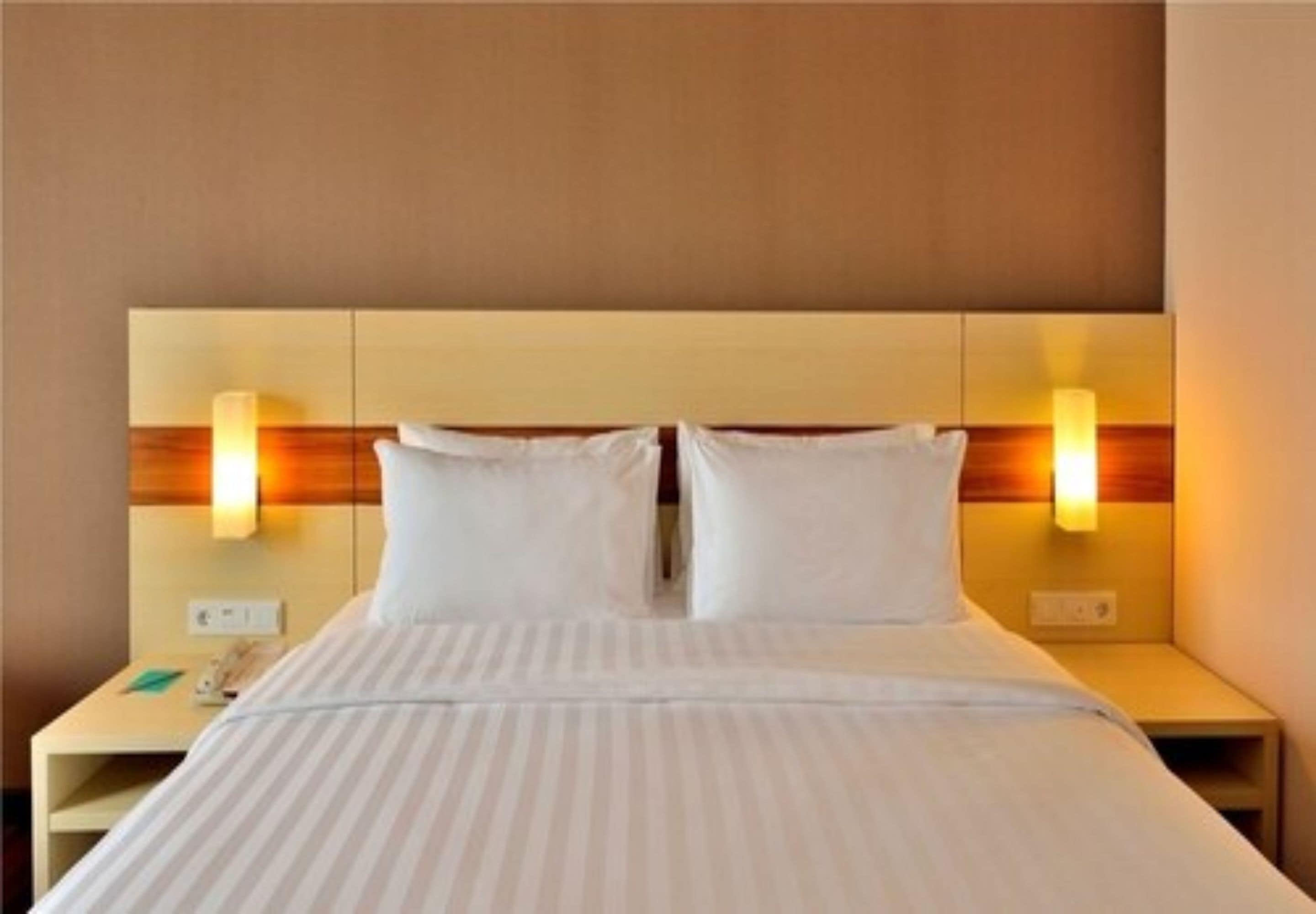 Una habitación de hotel con una cama grande, dos lámparas de noche y una mesita de noche con un teléfono.