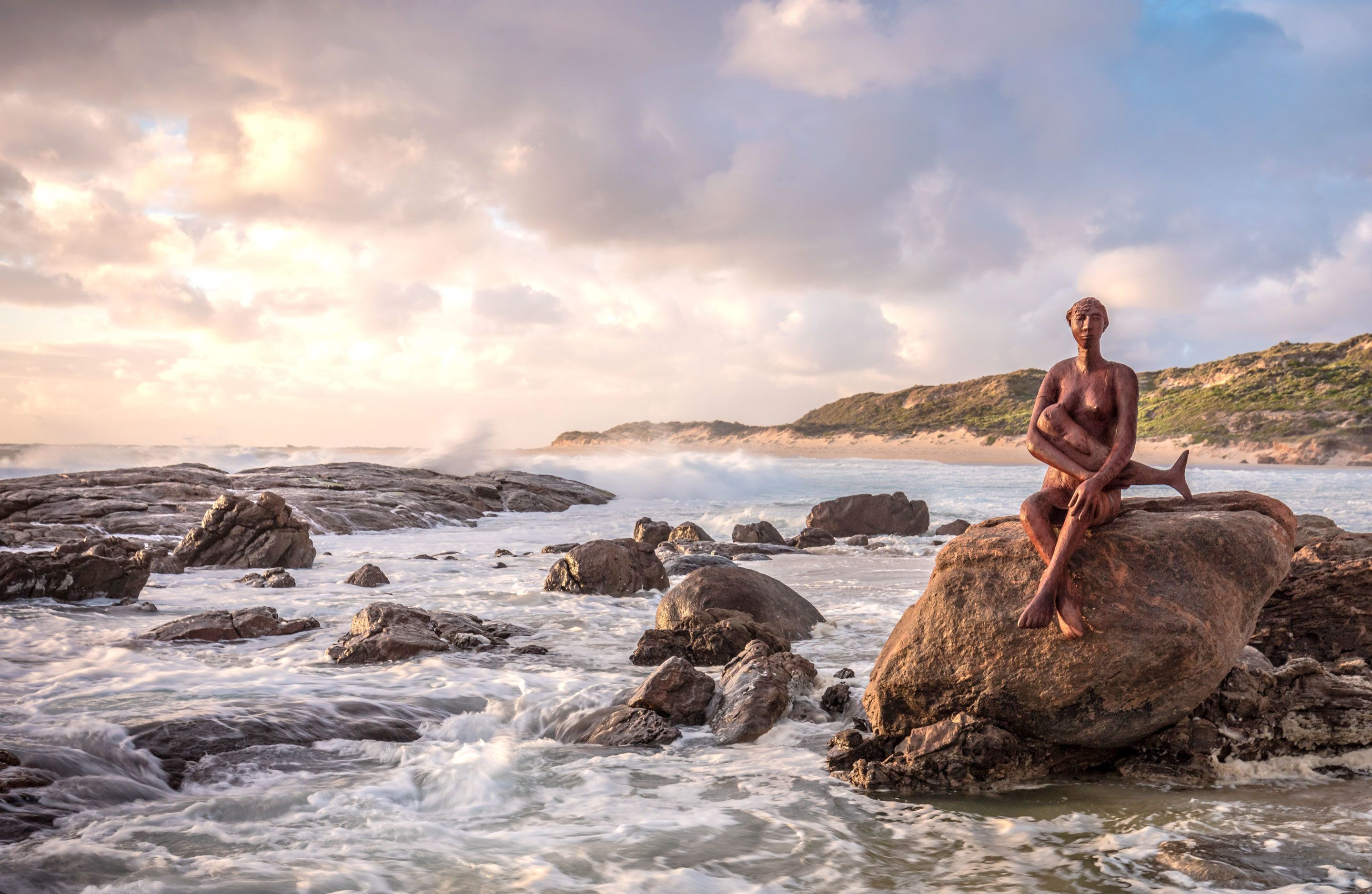 Una estatua de una figura sentada sobre una roca junto al mar.
