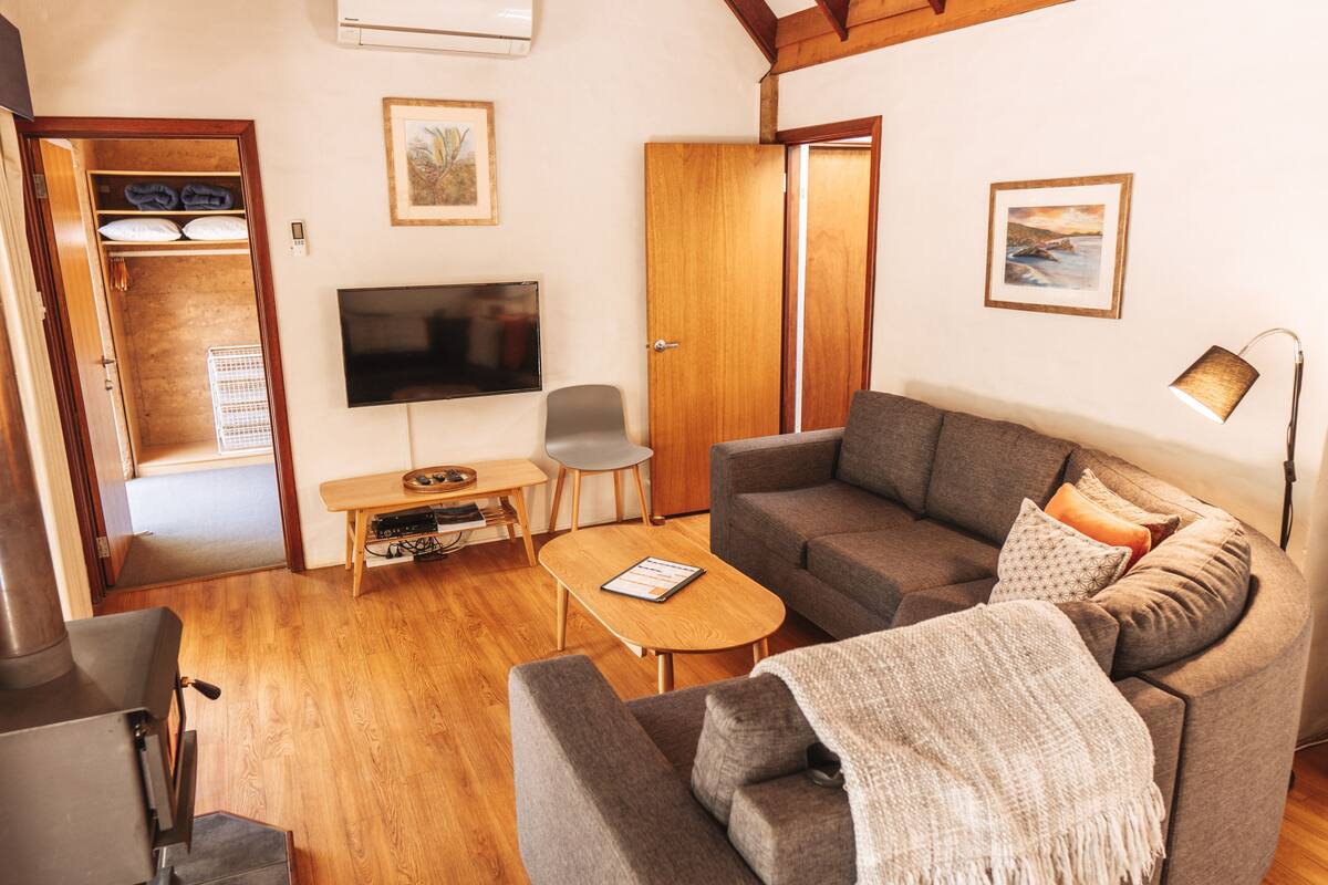 A cozy living room with a sofa, a coffee table, a TV, and a wooden floor.