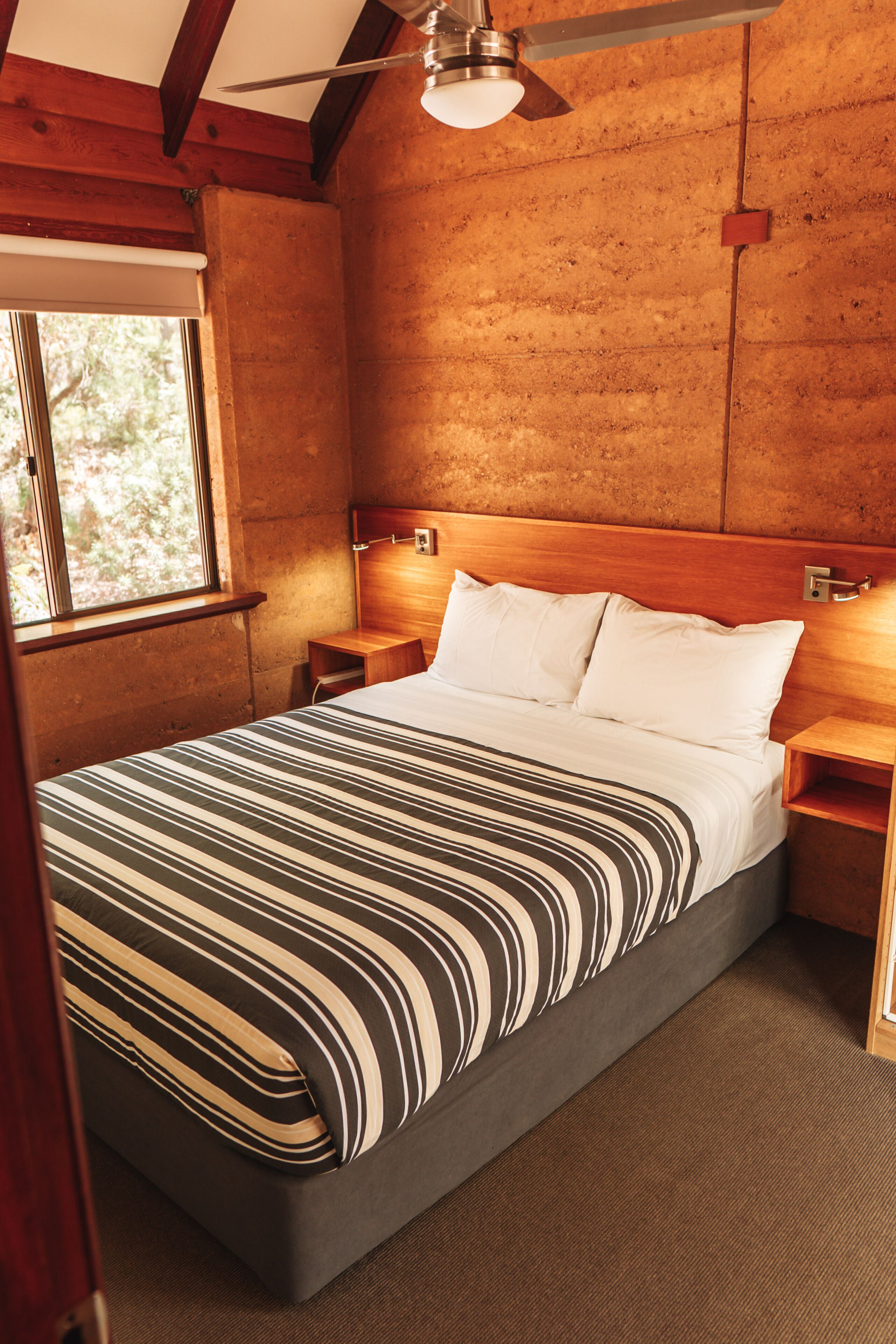 Um quarto com cabeceira de madeira, cama com roupa de cama listrada, ventilador de teto e mesa de cabeceira.