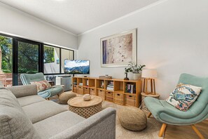 Una sala de estar moderna con un sofá, sillones, una mesa de centro, una estantería y un televisor.