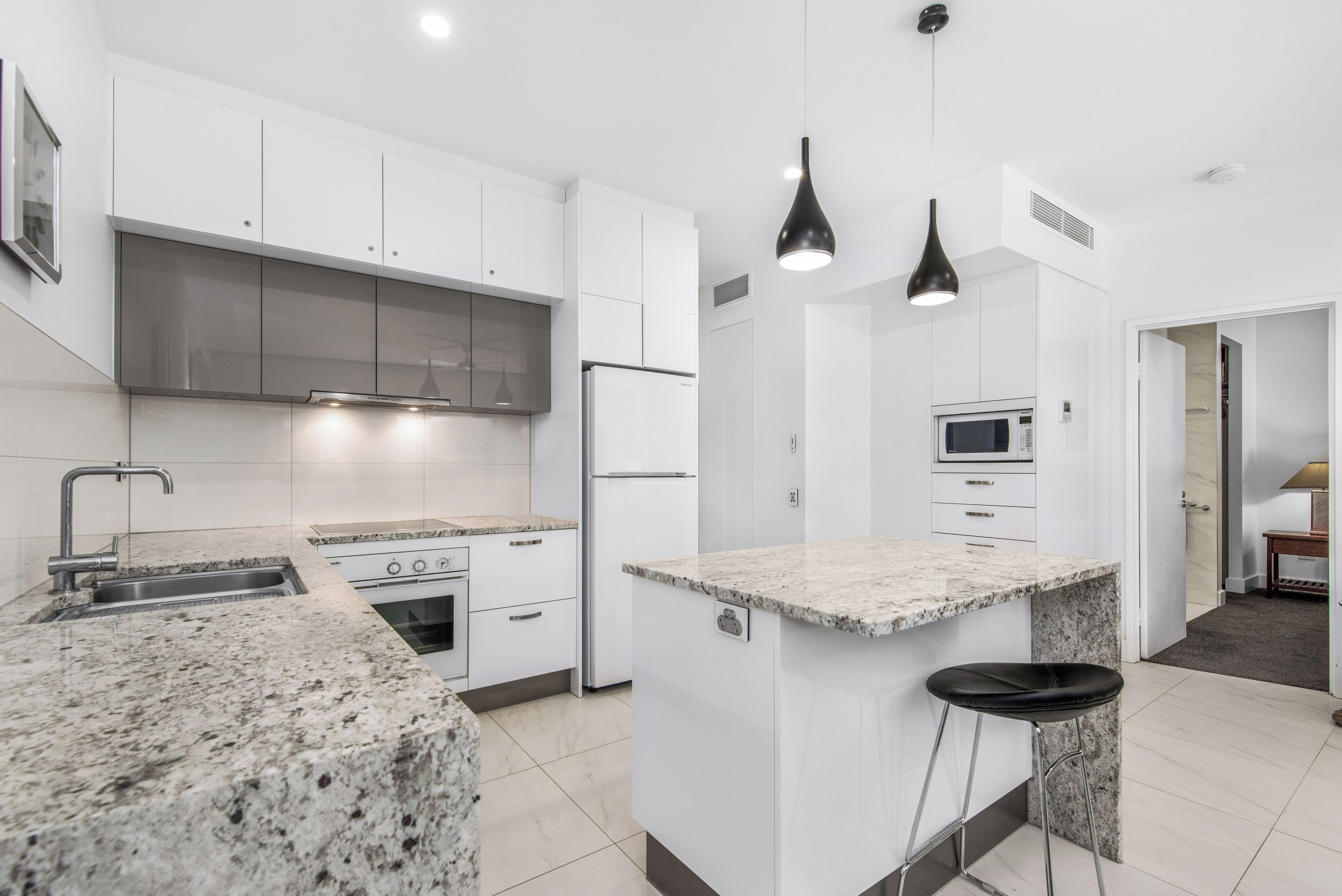 A modern kitchen with white cabinetry, a granite countertop, stainless steel appliances, and pendant lighting.