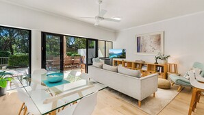 Uma sala de estar moderna com uma mesa de jantar de vidro, um sofá e um ventilador de teto.
