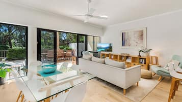 A modern living room with a glass dining table, a sofa, and a ceiling fan.