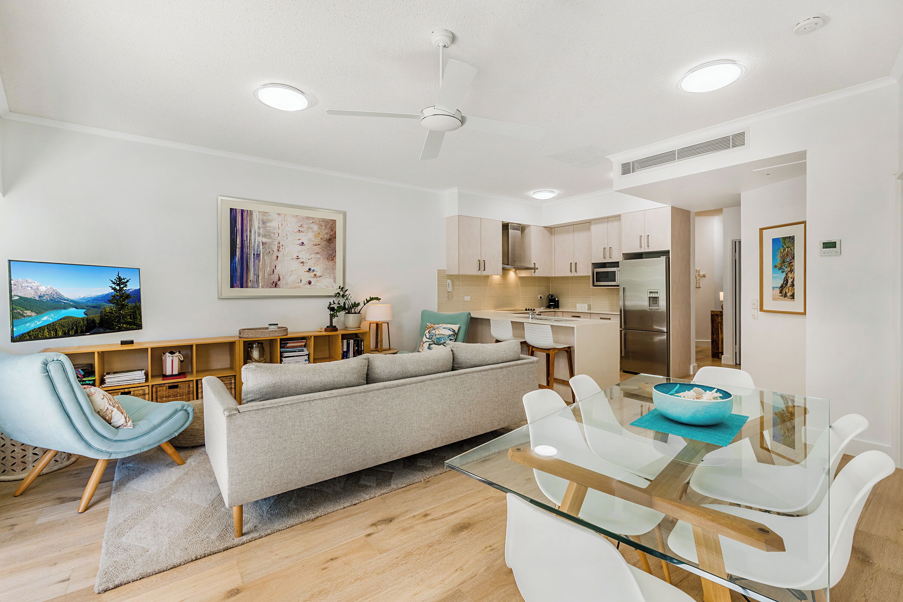A modern living room with a sofa, a glass dining table, and a kitchen in the background.