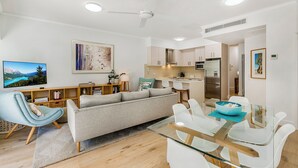 Uma sala de estar moderna com um sofá, uma mesa de jantar de vidro e uma cozinha ao fundo.