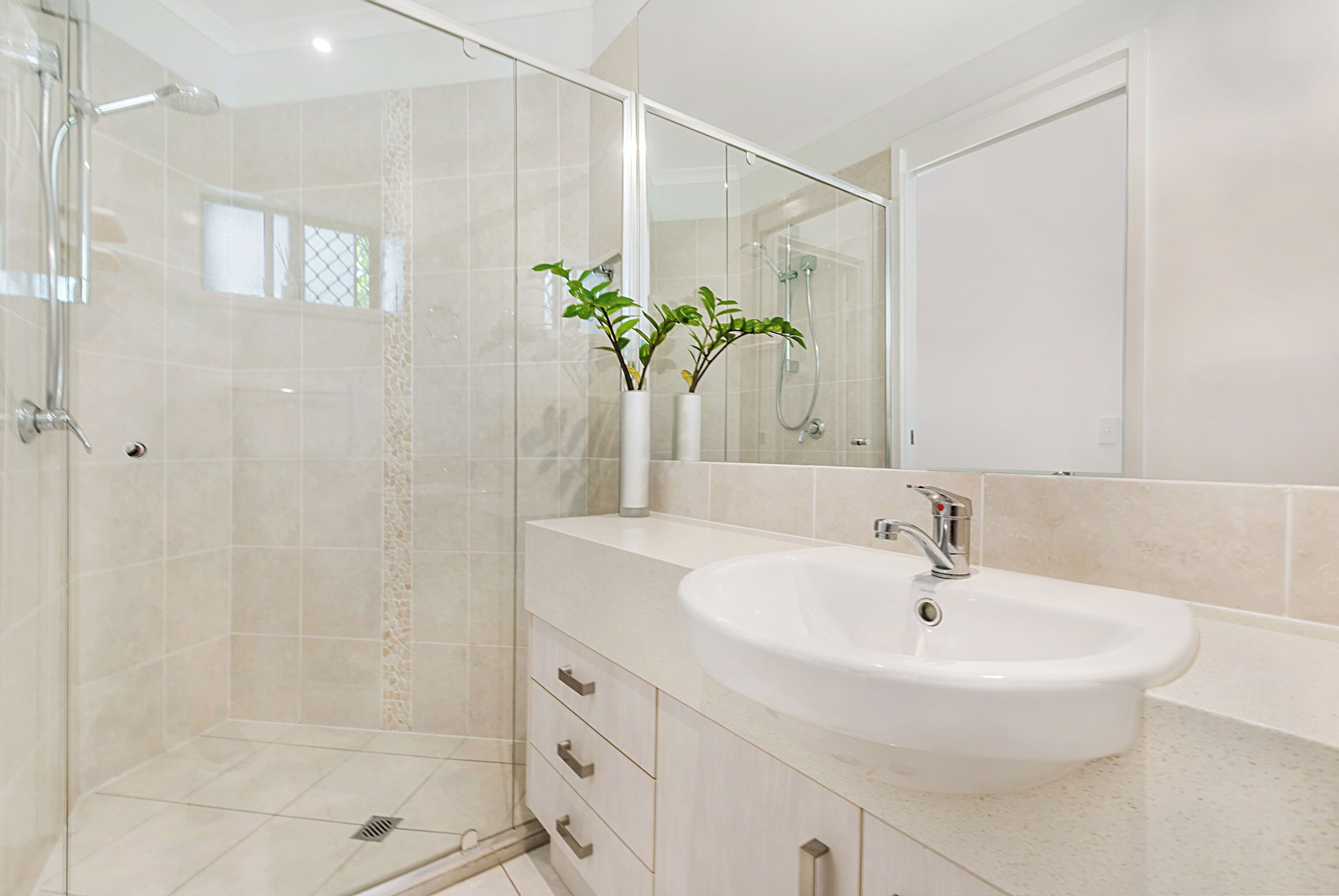 A modern bathroom with a glass-enclosed shower, a white sink, and a mirror above it.