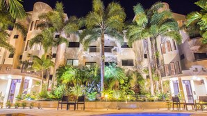 Um hotel com piscina, palmeiras e fachada bem iluminada.