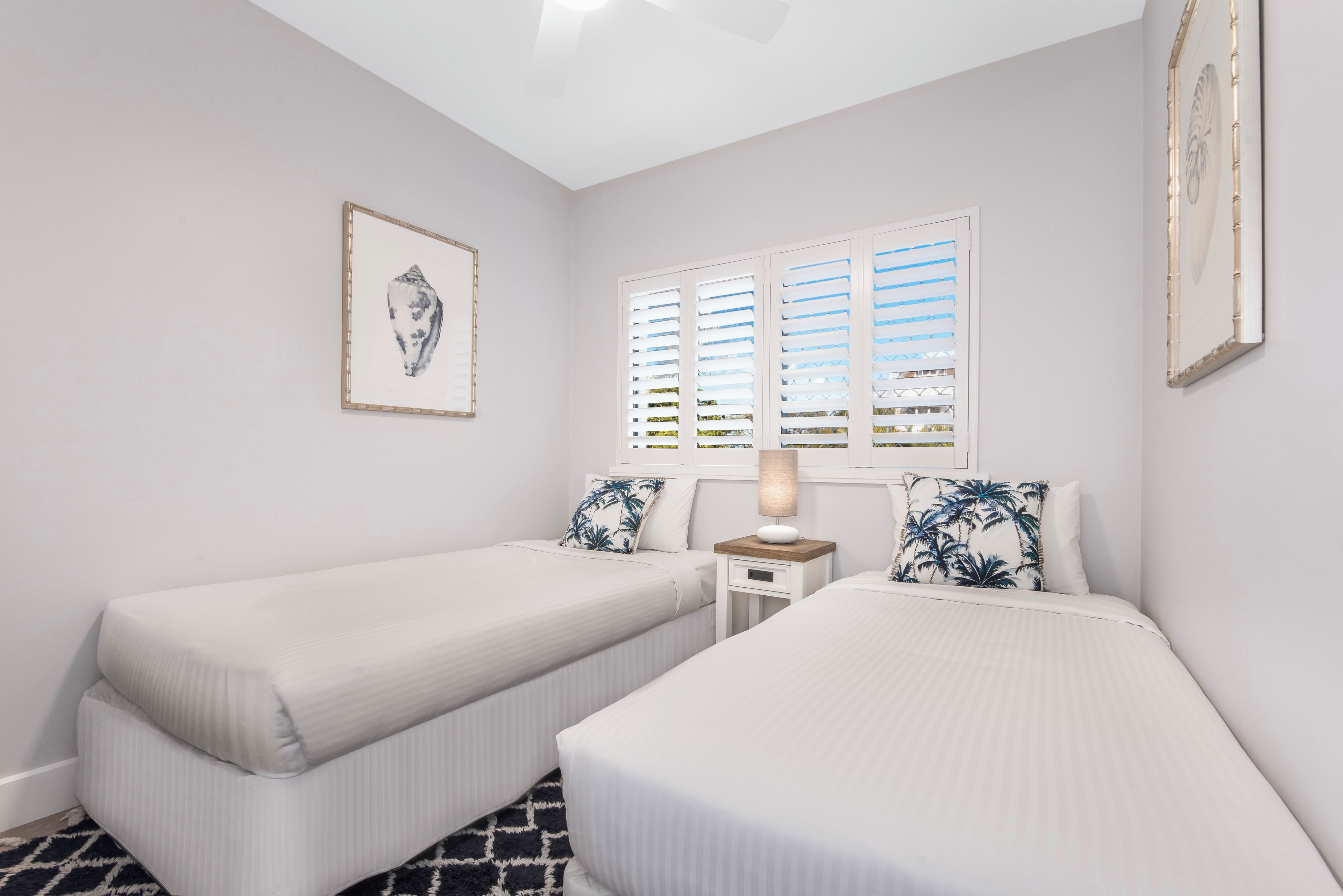Une chambre avec deux lits simples, une table de chevet avec une lampe et une fenêtre avec des volets.
