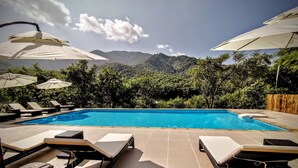 A swimming pool with lounge chairs and umbrellas, surrounded by lush greenery and mountains in the background. - Sanctuary Pakbeng Lodge (Pakbeng)