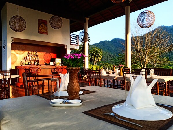 Un restaurante con terraza, zona de bar y vistas a las montañas.