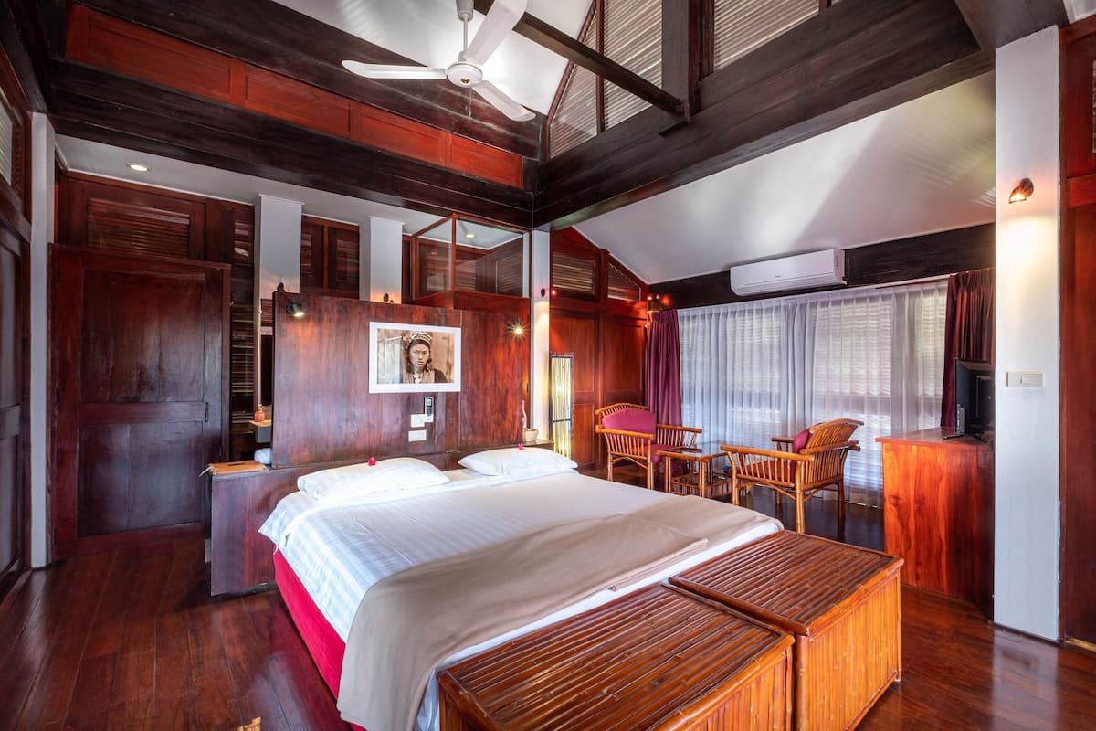 A hotel room with a large bed, wooden furniture, a desk, and a ceiling fan.
